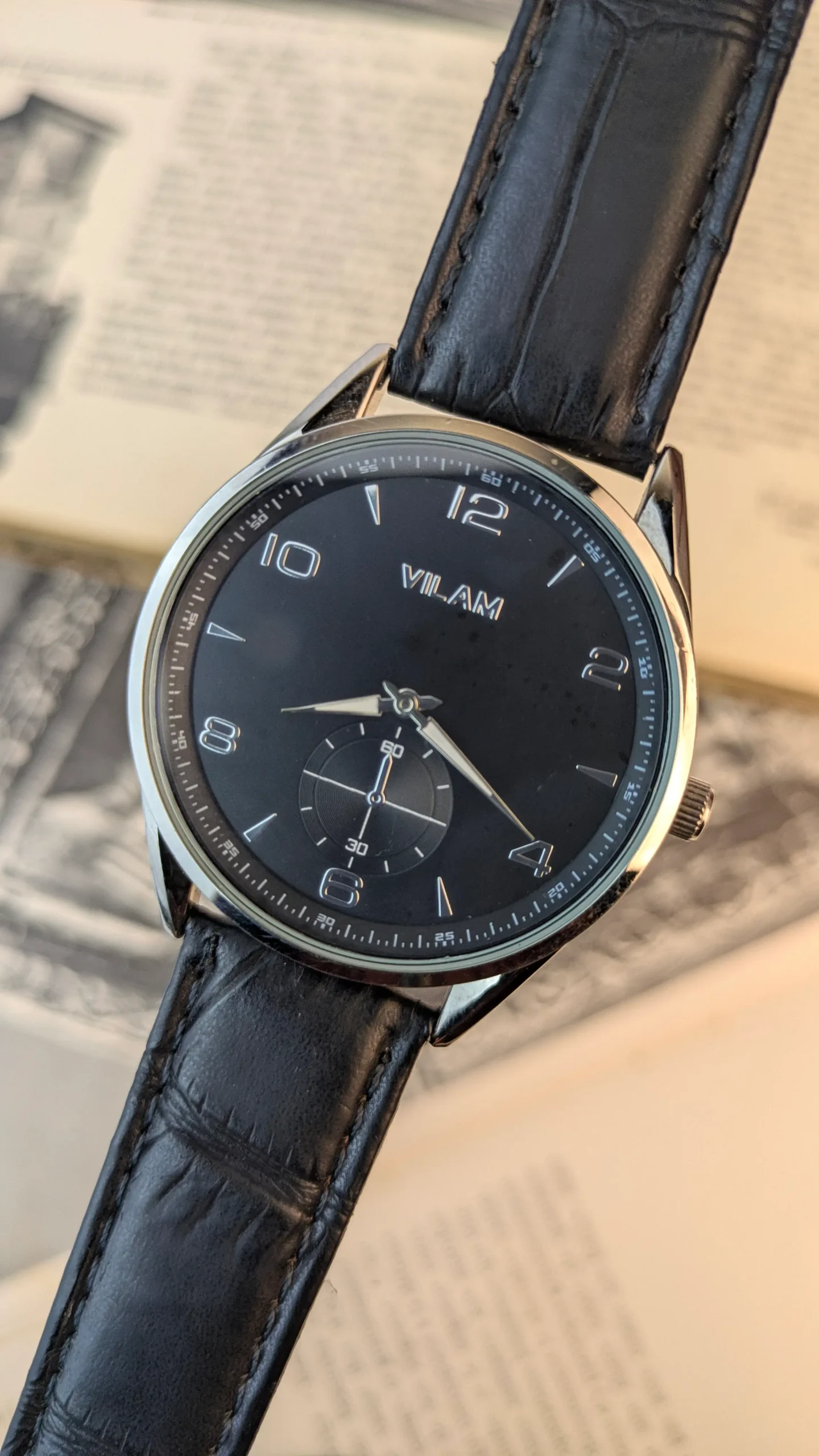 Vilam Classic black dial men's dress watch with sub-seconds complication and croco leather strap laid flat on vintage book