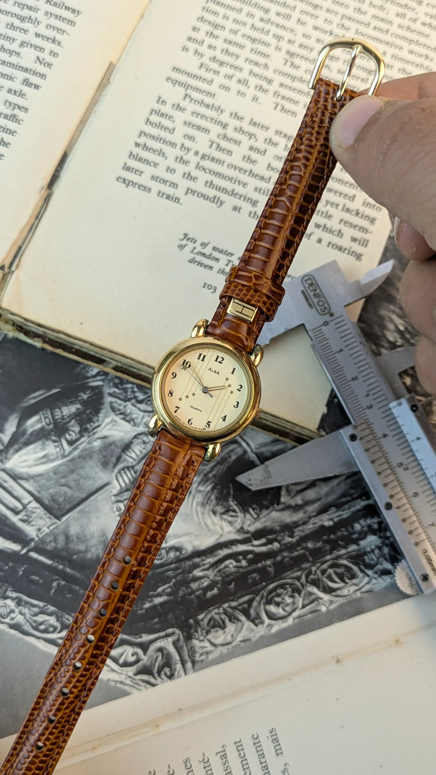 Full view of ALBA quartz watch placed beside a measuring caliper and book.