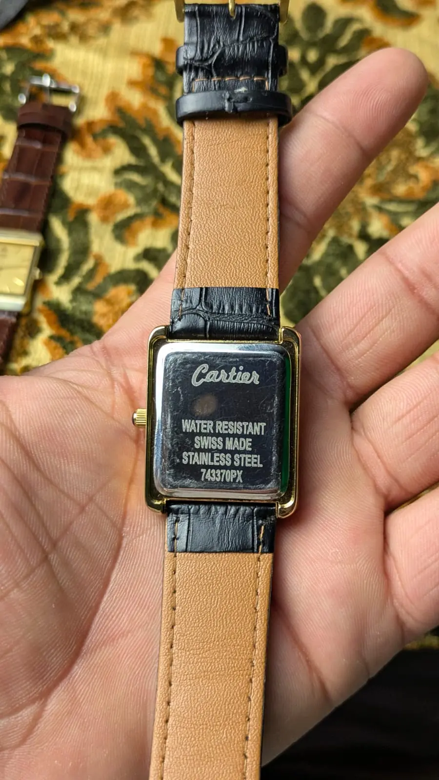 Back of Cartier full black dial gold frame watch showing stainless steel case and black leather strap